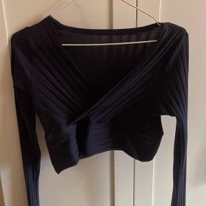 Svart omlottopp med ribbade detaljer - Snygg svart omlottopp med ribbade detaljer och croppad passform. Toppen har långa ärmar och en djup v-ringning framtill. Storlek L men sitter som en S/M mer