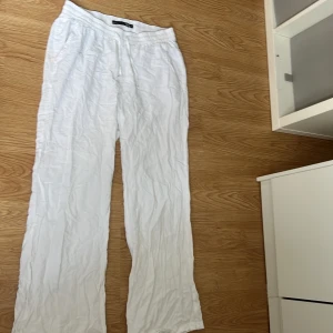 Vita linnebyxor med snörning, 157 - Vita linnebyxor från 157 med avslappnad passform och elastisk midja med snörning. Byxorna har raka ben, sidofickor och en bakficka. Perfekta för varma dagar när du vill ha en chill och luftig stil.