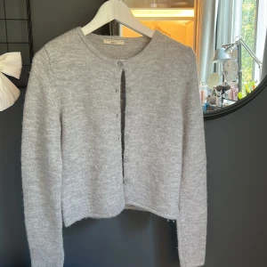 Ljusgrå kofta från Gina Tricot XS - Mysig ljusgrå kofta från Gina Tricot i storlek XS. Koftan är stickad med rund halsringning och har knappar framtill. Materialet är mjukt och fluffigt. Den är lite nopprig, använd 1-3 gånger. Ny pris 400kr.