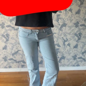 Ljusblå bootcut lågmidjade jeans - Säljer ett par ljusblå jeans med bootcut-modell och låg midja. Jeansen har klassisk femficksdesign och stängs med knapp och dragkedja. Perfekta för dig som gillar en retro vibe och vill ha ett par snygga jeans i stretchigt material.