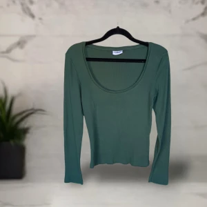Grön top från noisy may - Snygg grön långärmad topp från Noisy May med rund, djup urringning. Modellen är figurnära och i mjuk, ribbad bomull som sitter skönt på kroppen. Perfekt att styla med jeans eller kjol för en clean look.