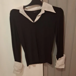 Svart tröja med vit krage Vero Moda - Stilren svart tröja från Vero Moda i storlek M med vit skjortkrage och vita uppvikta muddar. Tröjan har lång ärm och v-ringning, vilket ger en klassisk och trendig look. Perfekt för dig som gillar preppy stil.