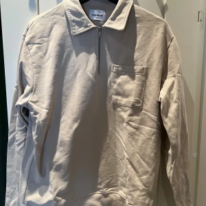 Beige half zip tröja från Woodbird - Snygg beige tröja från Woodbird i bomull med halv dragkedja och krage. Tröjan har en bröstficka med lock och långa ärmar. Perfekt för dig som gillar en clean och stilren look.