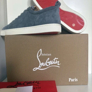 Christian Louboutin  - Snygga sneakers från Christian Louboutin i grå mocka med klassisk röd sula och vita kanter. Skorna har rund tå, snörning och diskret branding på sulan. Perfekta för dig som vill ha en stilren men lyxig look.