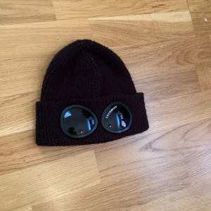 Svart mössa  - Cool svart mössa med deras ikoniska goggles framtill. Stickad i mjukt material och perfekt för att ge din outfit en unik touch. Passar dig som vill sticka ut och gillar streetwear-vibbar.