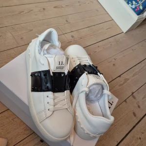 Valentino Opens Rockstud Untitled sneakers - Snygga vita Valentino Rockstud Untitled sneakers med svarta detaljer och ikoniska nitar på sidan. Skorna har rund tå, platt sula och snörning. Tillverkade i skinn med coola pyramidmönstrade nitar och en chunky vibe. Perfekt för dig som gillar statement pieces. Helt nya och aldrig använda endast testade inomhus.                                                   Kommer med dust bag och en Valentino påse.