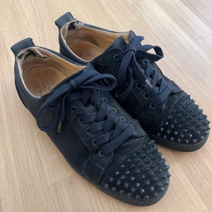 Christian Louboutin Louis Junior Spikes skor (43) - Blåa sneakers från Christian Louboutin i mocka med coola svarta nitar på tån och klassisk röd sula. Skorna har snörning och rund tå, vilket ger en edgy vibe. Perfekta för dig som vill sticka ut med en lyxig streetstyle-look.