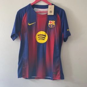 FC Barcelona matchtröja Nike M - Säljer en officiell FC Barcelona matchtröja från Nike i storlek M. Tröjan har klassiska blå och röda vertikala ränder, klubbmärke på bröstet, gul Nike-logga och Spotify som sponsor. Tillverkad i lätt och ventilerande polyester, perfekt för fotboll eller supporterliv.