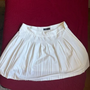 Vit plisserad kjol från FB Sister - Superfin vit plisserad kortkjol från FB Sister i storlek XL. Känns mer som en storlek M.Kjolen har klassiska veck och stängs med knapp i sidan. Perfekt för en trendig och sportig look, lätt att matcha med sneakers eller boots.