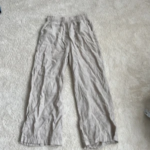 Beiga linnebyxor från Gina Tricot - Snygga beiga linnebyxor från Gina Tricot i storlek 34. Byxorna har resår i midjan med dragsko och raka, vida ben. Lätta och luftiga i materialet linne.