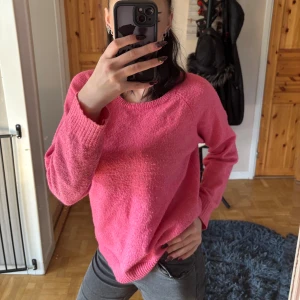 Rosa stickad tröja med rund hals - Mysig rosa stickad tröja med rund halsringning och långa ärmar. Tröjan har en relaxed passform och ribbade muddar vid ärmslut och nederkant. Perfekt för lager-på-lager under kyligare dagar.