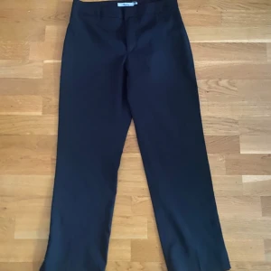 Svarta capri kostymbyxor - Klassiska svarta capri kostymbyxor från Attention i storlek 38. Byxorna har rak passform, hög midja och stängs med hake och dragkedja.  Materialet känns mjukt och följsamt. 97% polyester och 3% elastic, sparsamt använda! Made in Greece, finns inga fel! 