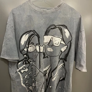 Grå t-shirt med print från Zara - Grå t-shirt från Zara med coolt grafiskt print av två personer med stora solglasögon och pärldetaljer på framsidan. T-shirten har rund hals, korta ärmar och en avslappnad passform. Perfekt för dig som gillar unika statement-plagg.