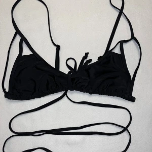 Svart bikiniöverdel med snörning - Snygg svart bikiniöverdel med tunna axelband och långa snören som kan knytas runt midjan. Klassisk trekantsmodell med justerbara band för perfekt passform. Perfekt för stranden eller poolen, enkel att matcha med olika underdelar.
