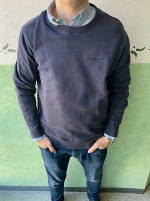 Mörkblå sweatshirt från J.Lindeberg - Snygg mörkblå sweatshirt från J.Lindeberg i storlek L. Tröjan har rund hals, diskret broderad logga på bröstet och långa ärmar. Tillverkad i mjuk bomull som är skön mot huden. Perfekt för chill dagar och enkel att matcha med jeans eller joggers.