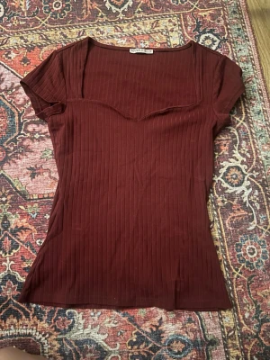 Ribbad vinröd topp från Anna Field - Säljer en vinröd ribbad topp från Anna Field med korta ärmar och snygg sweetheart-urringning. Toppen har en slim passform och är tillverkad i mjukt material som sitter skönt mot kroppen. Perfekt att styla med jeans eller kjol.