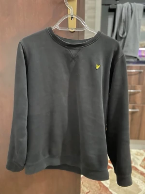Svart sweatshirt från Lyle & Scott - En stilren svart sweatshirt från Lyle & Scott Junior med klassisk rund hals och den ikoniska gula logon broderad på bröstet. Tröjan har långa ärmar och är gjord i mjuk bomull för maximal komfort. Finns även en till Lyle Scott tröja i nyare skick exakt likadan för 250 kr men är öppen för bud!