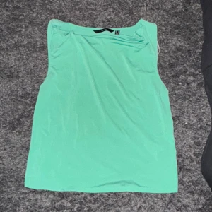 Mintgrön ärmlös topp från Vero Moda - Snygg mintgrön topp från Vero Moda i storlek M. Toppen är ärmlös med en draperad halsringning som ger en cool och modern look. Materialet är mjukt och stretchigt, perfekt för varma dagar. Aldrig använd! Prislapp sitter kvar:)