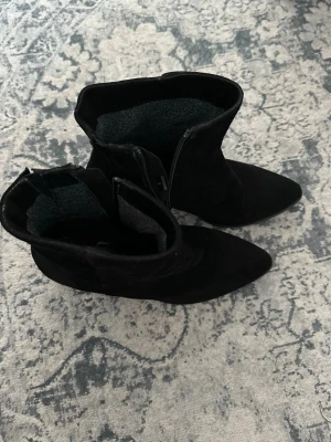 Svarta boots med spetsig tå från ELLA - Säljer ett par svarta stövletter från ELLA med snygg spetsig tå och klack. Bootsens utsida är i mocka och de har dragkedja i sidan. Skorna är lätt fodrade så funkar också att ha nu i vinter ❄️ Passar perfekt till nyår eller mer uppklätt till vardags. Orginalpris ca. 1000