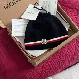 Svart mössa med röd-vit rand - Säljer en svart mössa med klassisk logga framtill och snygga ränder i vitt och rött längs kanten. Mössan är ribbstickad och kommer i originalförpackning med tags kvar. Perfekt för dig som vill ha en stilren accessoar med lyxig känsla.