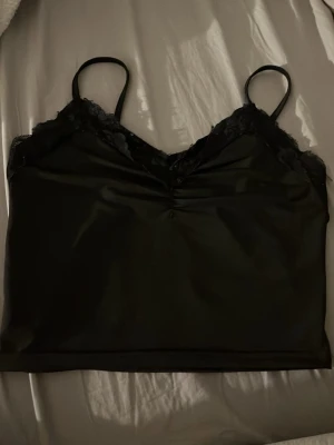 Svart satin linne med spets - Snygg svart linnetopp  med tunna axelband och spetsdetaljer vid v-ringad hals. 