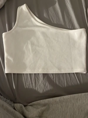 Vit ribbad oneshoulder topp - Säljer en vit ribbad topp med oneshoulder-design. Använd fåtal gånger 