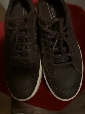 Bruna sneakers från Ecco med vit sula - Säljer ett par bruna sneakers från Ecco med snygg vit platt sula och rund tå. Skorna har snörning och är tillverkade i skinn med diskreta sömmar och detaljer. Perfekt för dig som gillar stilrena och bekväma skor med dansk design.