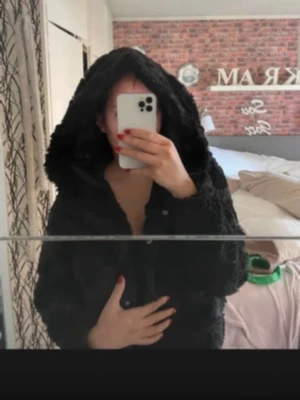 Svart teddyjacka från Vero Moda - Mysig svart teddyjacka från Vero Moda i storlek M. Jackan har en stor huva och stängs med knappar framtill. Perfekt för dig som vill ha en fluffig och trendig look under kyliga dagar.