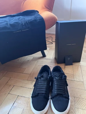 Svarta sneakers från Giuseppe Zanotti - Säljer ett par sällsynta svarta sneakers från Giuseppe Zanotti köpta från Farfetch. Med vit platt sula, grov snörning och dragkedjor på sidorna. Använda ungefär 6 ggr. Allt originellt ingår