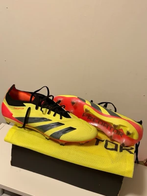 Adidas Predator fotbollsskor gul/svart - Adidas Predator fotbollsskor i en fet gul färg med svarta och röda detaljer. Skorna har snörning, platt sula med dobbar och en rund tå. Ovandelen är i syntetmaterial och insidan är röd med Predator-tryck. Perfekt för dig som vill sticka ut på planen dom är storlek 44 helt nya aldrig använda säljer då dom är lite stora köpta för 2399 på rea men säljer dom och vill ha sålt dom nu så därav det låga  priset 😁.