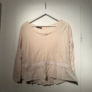 Blus - En cremevit / ljusrosa blus med knappar i ryggen och volang nertill 