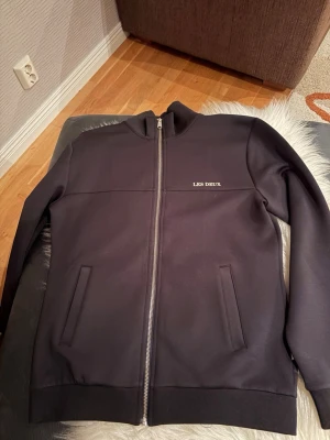 Svart zip-kofta från Les Deux - Snygg svart kofta från Les Deux med hel dragkedja framtill och diskret logga på bröstet. Modellen har ribbade muddar, två fickor och en stilren, normal passform. Perfekt till jeans och t-shirt för en chill look. Tröjan är använd ett fåtal gånger, skriv vid minsta fundering🙌🏻🙌🏻