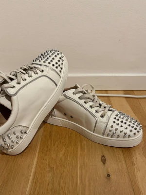 Vita loubs med spikar bak o fram - Säljer ett par sjukt snygga vita sneakers från Christian Louboutin med silverfärgade nitar på tå och häl. Mycket bra skick, men ska tvätta innan frakt. Storleken 42, passar även 43. Köpta här hemma p plick så är osäker på äkthet, därav pris. Box och dustbag medföljer.