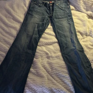 Divide bootcut jeans med nitar - Snygga blå bootcut jeans med coola nitar på fram- och bakfickorna. uppsydda i midjan. 39cm rakt över midjan. 85cm i innerbenslängd 