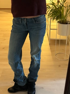 Blåa raka jeans från wrangler - Säljer ett par klassiska blå jeans från wrangler.De har låg midja, raka ben och fem fickor. Jeansen är i mjukt denimtyg med snygg tvätt och subtila slitningar. Passar perfekt till sneakers och en avslappnad stil.