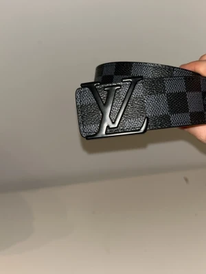 Svart rutigt bälte  - Bältet är väldigt fint och passar med flera olika klädesplagg. Den är rutig och har ett stort märke i mitten 