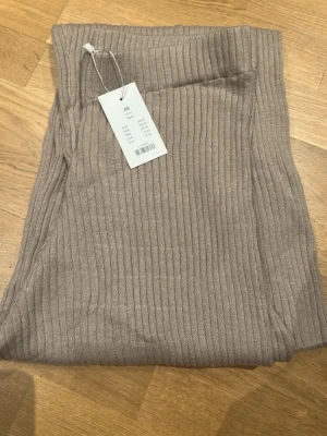Beige ribbade byxor i stickat material XS - Säljer ett par beige ribbade byxor från 157 i stickat material. Byxorna har hög midja och raka, lite vidare ben. Perfekta för en chill och avslappnad look. Supermjuka och sköna att ha på sig.