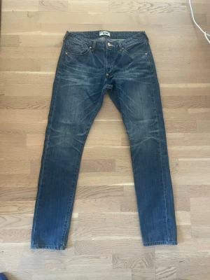 Blå jeans från Acne Studios - Säljer ett par snygga blå jeans från Acne Studios med klassisk femficksdesign och kopparfärgade nitar. Jeansen har en rak passform och är tillverkade i slitstarkt denimtyg. Perfekta för dig som gillar stilrena och tidlösa jeans.storlek 28/32
