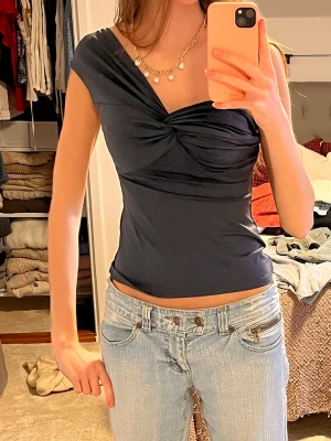 Mörkblå omlott topp med twist - Säljer en mörkblå omlott topp med snygg twistad detalj framtill. Toppen har offshoulder och kan även bäras med kort ärm, vilket ger en flexibel look. Materialet är mjukt och strecthigt. Man kan bära den på olika sätt 