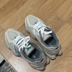 Beige New Balance sneakers - Säljer ett par snygga New Balance sneakers i beige och grått med vita snören och detaljer i silver. Skorna har en chunky sula med svarta och mintgröna inslag undertill. Ovandelen är i mesh och mocka, med den klassiska N-loggan på sidan.