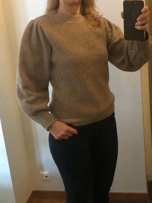 Beige stickad tröja med puffärm - Säljer en beige stickad tröja från Mango med ribbad struktur och puffiga långärmar. Tröjan har rund hals och breda muddar vid ärmslut och nederkant. 