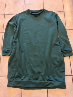 Mörkgrön sweatshirtklänning 1XL - En enkel och cool mörkgrön sweatshirtklänning i storlek 1XL. Klänningen har rund hals, långa ärmar och är tillverkad i mjuk polyester med lite stretch från spandex. Perfekt för en avslappnad och chill stil.