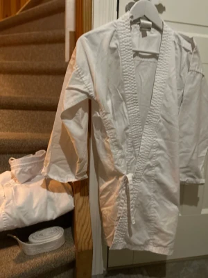 Karate-/judodräkt 150 - Bilderna visar en vit karate- eller judodräkt från Outshock i storlek 150 cm, med tillhörande bälte. 