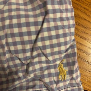 Rutig Polo Ralph Lauren shorts M - Säljer ett par rutiga shorts från Polo Ralph Lauren i storlek M. De har blått och vitt rutmönster, gul elastisk midja och klassisk Polo-logga broderad i gult. Materialet är bomull med meshfoder, perfekt för chill dagar. Bakficka med knapp och snygga detaljer.