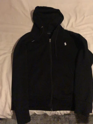 Svart Polo Ralph Lauren zip up -   🔥 Svart Polo jacka 🔥 Riktig clean Polo-jacka i helsvart – en statement-piece som funkar till allt. Grym passform, skön att bära och lätt att styla både casual och mer dressed. Sparsamt använd och i mycket fint skick ✅  Perfekt för höst/vår men funkar året runt. Snabb leverans 📦 💨 