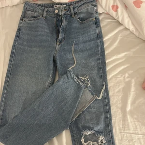 Blå ripped jeans från Zara - Säljer ett par blå jeans från Zara med snygga slitningar och hål på båda benen. Klassisk femficksmodell med dragkedja och knapp framtill. Jeansen är utsvängda och har en hög midja. Använda en gång💕