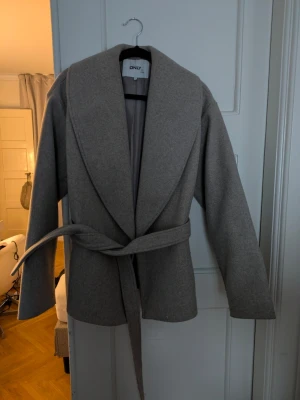 Beige kappa från ONLY med bälte - Säljer en stilren beige kappa från ONLY i storlek S, passar även M Jackan har bred krage, knytskärp i midjan och är helfodrad. 