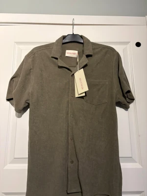 Armygrön terry skjorta Revolution M - Nypris: 700kr / Armygrön skjorta från Revolution i mjukt frottématerial. Modellen är Terry Cuban Shirt med korta ärmar, klassisk krage, bröstficka och knappar framtill. Perfekt för dig som gillar streetwear och nostalgi.