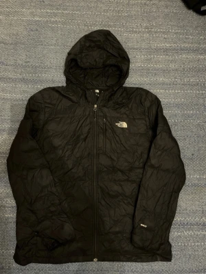 Svart vindjacka från The North Face XXL Men - Svart vindjacka från The North Face i storlek XXL. Jackan har huva, hel dragkedja framtill och två sidofickor. Tillverkad i lätt och slitstark polyester, perfekt för blåsiga dagar. Klassisk logga på bröstet och enkel, stilren design.