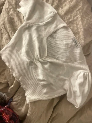 Vit ribbad croppad topp från Dilvin - Säljer en vit croppad topp från Dilvin med ribbad struktur och puffiga korta ärmar. Toppen har en snygg v-ringning med rynkade detaljer framtill som ger en cool look. Perfekt att styla med höga jeans eller kjol.